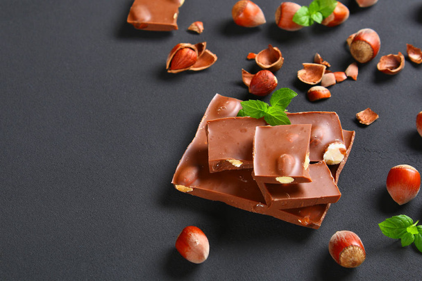Suklaa hasselpähkinöillä, mintulla ja kahvinjyvillä tummanharmaalla pöydällä
 - Valokuva, kuva