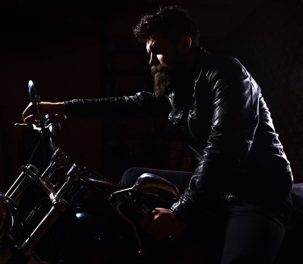 Macho, brutal biker in leather jacket riding motorcycle at night time, copy space. Man with beard, biker in leather jacket sitting on motor bike in darkness, black background. Night racer concept - Foto, Imagen