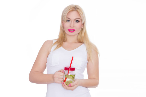 A friendly blond woman holds a glass of water and lime in her hands. A girl is drinking lemonade. Concept - healthy food, thirst quenching in summer - Photo, Image