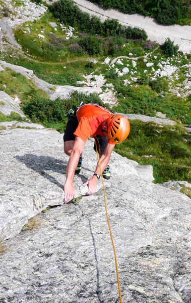 kalliokiipeilijä pukeutunut kirkkaisiin väreihin jyrkällä graniittikiipeilyreitillä Alpeilla
 - Valokuva, kuva