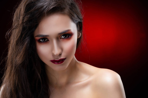 Portrait of a beautiful glamorous brunette girl with naked shoulders. Shimmering makeup, red lips. Healthy smooth skin. Black and red background. Copy space. Commercial and advertising design. - 写真・画像