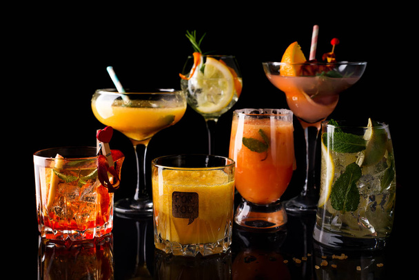 Cóctel whisky-cola, mojito-cóctel, cóctel naranja, cóctel de fresa en vasos de cristal con pajitas aisladas en negro
, - Foto, imagen