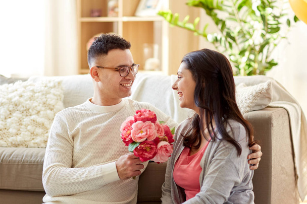 happy husband giving flowers to his wife at home - Foto, imagen