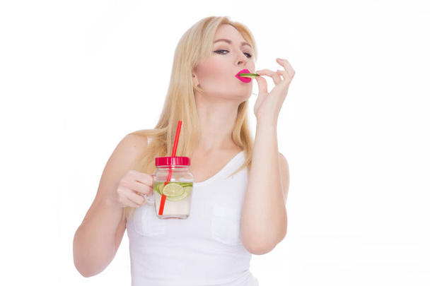 A woman on a white background holds a glass with lemonade in one hand, and in the second hand holds a piece of lime - Foto, Bild