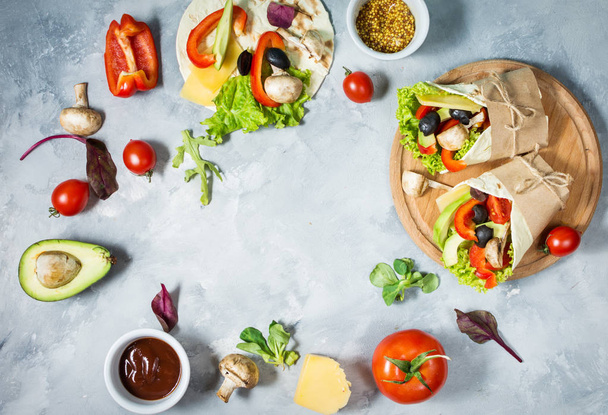 Lanche saudável vegan almoço. Tortilla envolve com cogumelos, legumes frescos e ingredientes em fundo de concreto. Vista superior
 - Foto, Imagem
