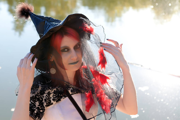 young witch in pointed black hat near river - Фото, изображение