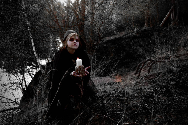 witch in forest wearing black cape with candles and skull - Fotoğraf, Görsel