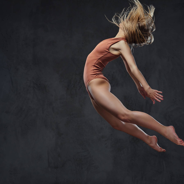 Jovem bailarina graciosa dança e salta em um estúdio. Isolado em um fundo escuro
. - Foto, Imagem