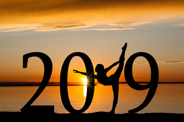 2019 New Year silhouette of a girl dancing or exercising at the beach during golden sunrise or sunset with copy space. - Photo, Image