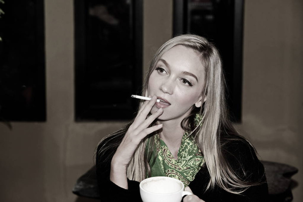 Piękna dziewczyna jest palenie na zewnątrz kawiarni. - Zdjęcie, obraz