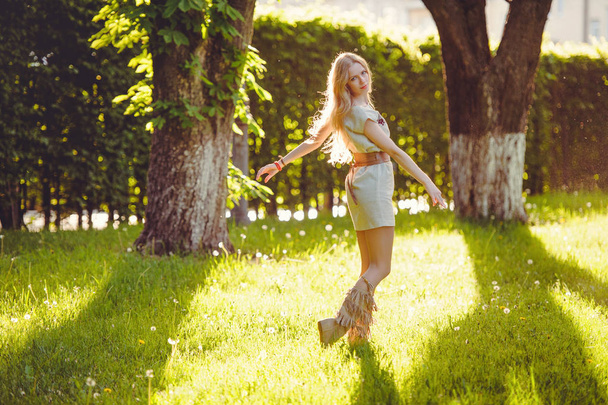 ніжна жінка блондинка йде по траві на тлі вечірнього сонця, одягнена в натуральне етнічне плаття, стильно і затишно. Поняття любові природи
. - Фото, зображення