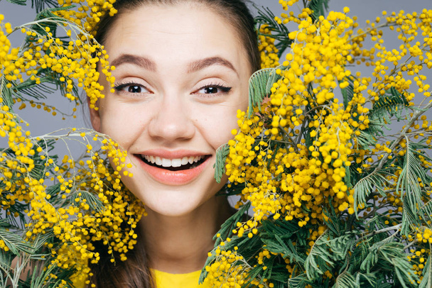 a cute young girl rejoices in the spring and laughs, holds a fragrant yellow mimosa - Photo, image
