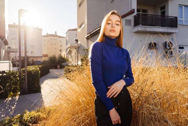 beautiful stylish girl blond model in blue sweater posing on city streets in the sun - Photo, Image