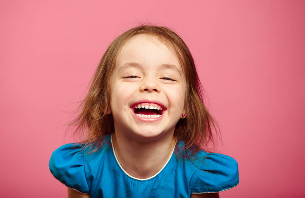 Frontalaufnahme des lachenden fröhlichen kleinen Mädchens steht neben rosa Wand. - Foto, Bild