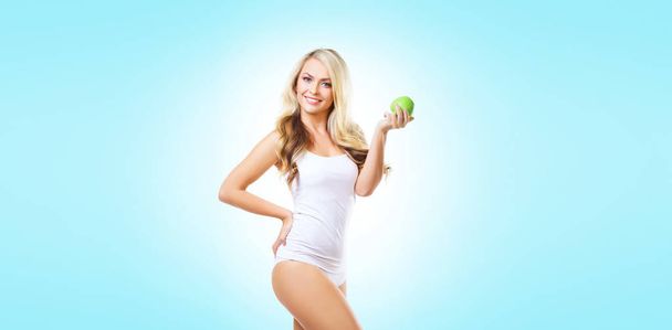 Dopasowanie i sportowy dziewczyna w białej bieliźnie. Piękne i zdrowe kobiety jedzenie zielone jabłko na błękitnym tle. Sport, fitness, diety, odchudzanie, odżywianie i koncepcji opieki zdrowotnej. - Zdjęcie, obraz