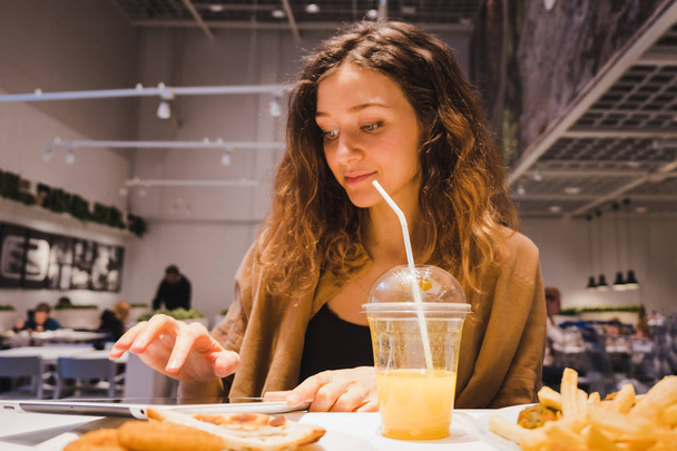 Όμορφη γυναίκα χρησιμοποιεί ένα δισκίο σε ένα γρήγορο φαγητό καφέ και ποτά χυμό - Φωτογραφία, εικόνα
