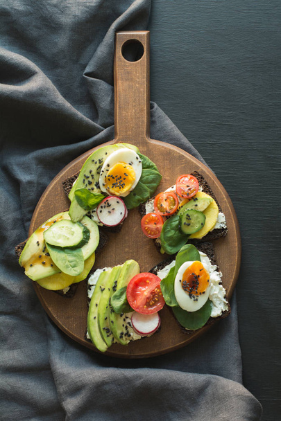 Different sandwiches with vegetables, eggs, avocado, tomato, rye bread on black chalkboard background. View from above. Appetizer for party. Flat lay. - Zdjęcie, obraz