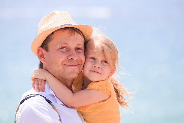Happy little girl hugging father. Cheerful young man with child close-up on sea background. Happy family theme. - Photo, Image