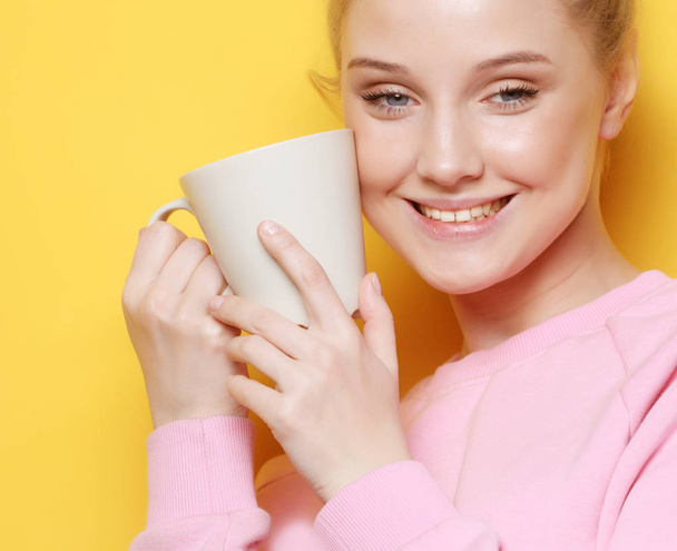 Young blond woman holding white cup with tea or coffee, lifestyle and food concept. Close up. Yellow background. - Valokuva, kuva