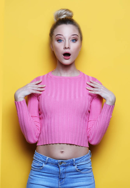 Surprised young blond woman shouting over yellow background. Looking at camera. - Photo, Image