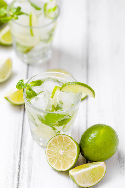 Summer refreshing cocktail mojito with lime and mint on white wooden vintage background. Fresh summertime iced drink with green citrus and fragrant leaves in beautiful glasses. - Foto, immagini