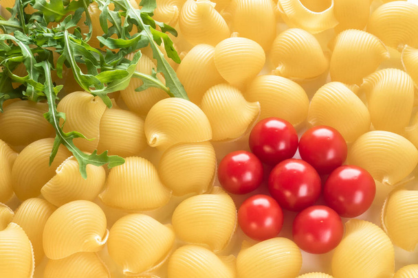 Food background Uncooked Macaroni Lumaconi close-up macro red Cherry Tomatoes in flower form and leaves Rucola Salad Concept set of ingredients for Pasta - Foto, afbeelding