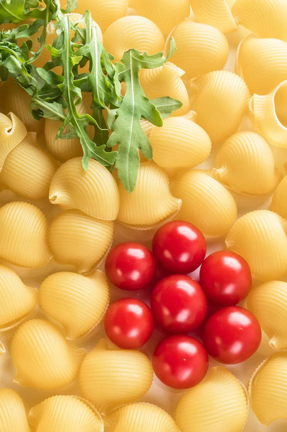 Food background Uncooked Macaroni Lumaconi close-up macro red Cherry Tomatoes in flower form and leaves Rucola Salad Concept set of ingredients for Pasta - Foto, immagini