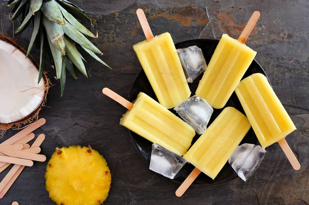 Pineapple coconut ice pops on a plate. Top view scene over a dark slate background. - Photo, Image
