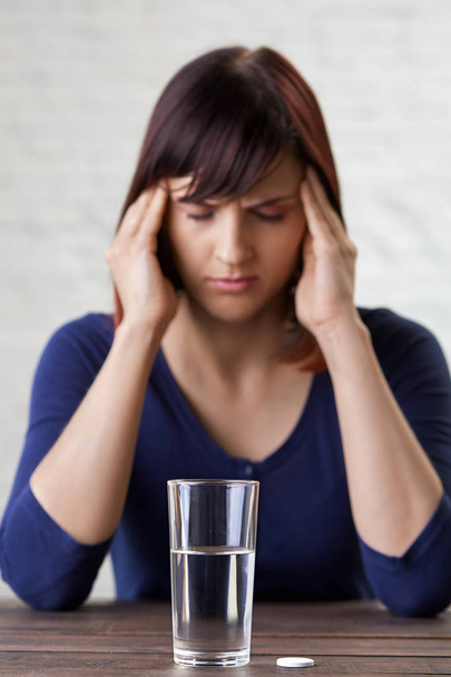 Mladá žena trpí silnou bolestí hlavy, držení prsty na spánky a zavírání oči od bolesti, připravované užívat lék. Těžká migréna. Aspirin - Fotografie, Obrázek