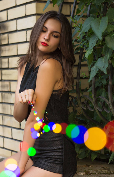 Pretty brunette girl with red lips holding garland at the city park - Фото, зображення