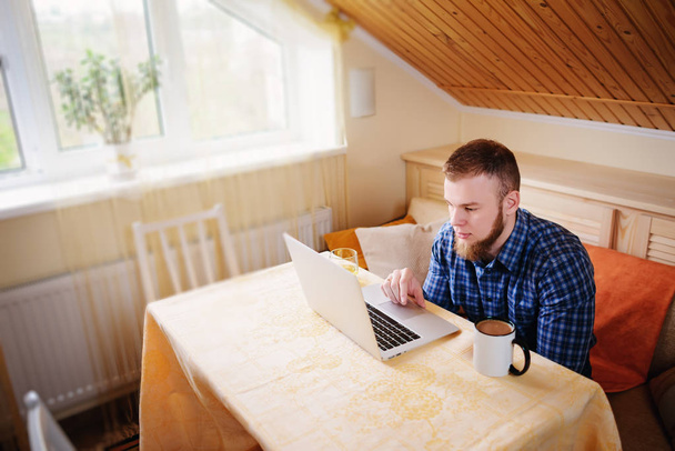 entspannter junger Profi surft im Internet auf seinem Laptop in einem Esszimmer. - Foto, Bild