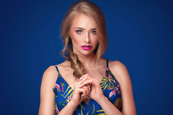 Beautiful blonde young woman with glamour makeup and braid hairstyle posing on blue background. - Photo, image