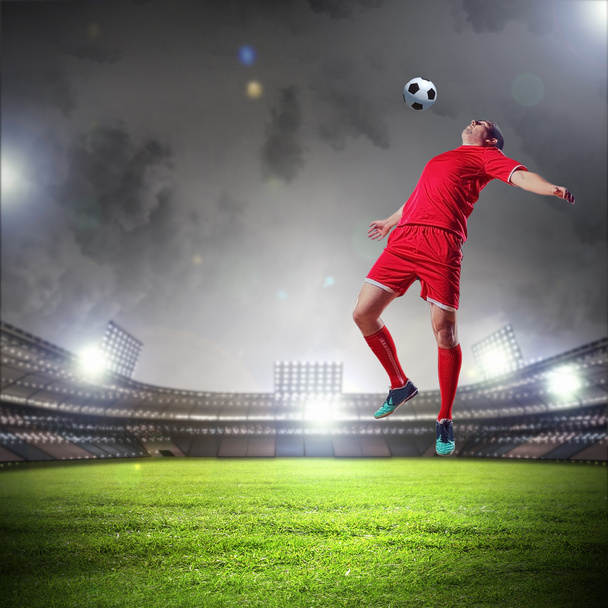 Football player in red shirt striking the ball at the stadium - Фото, изображение