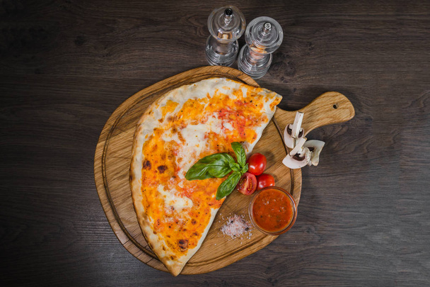 Hot piece of pizza with melted cheese on a rustic wooden table - Zdjęcie, obraz