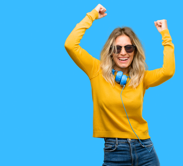 Young beautiful woman with headphones happy and excited celebrating victory expressing big success, power, energy and positive emotions. Celebrates new job joyful - Photo, Image