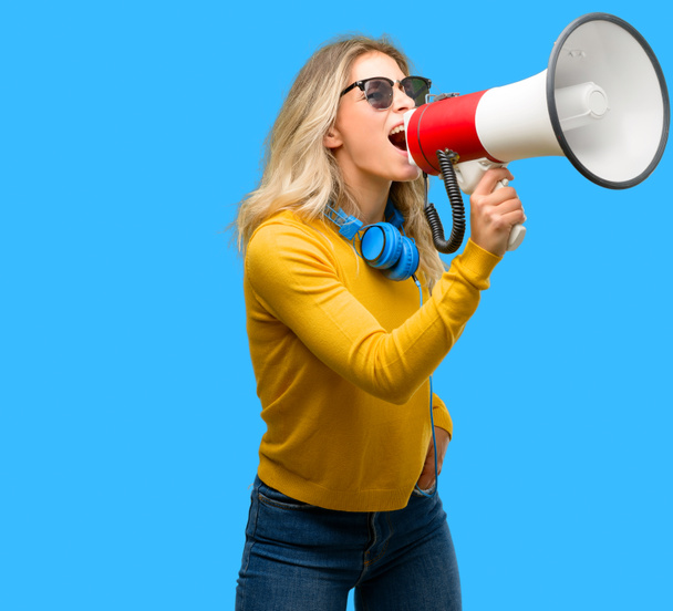 Young beautiful woman with headphones communicates shouting loud holding a megaphone, expressing success and positive concept, idea for marketing or sales - Photo, Image