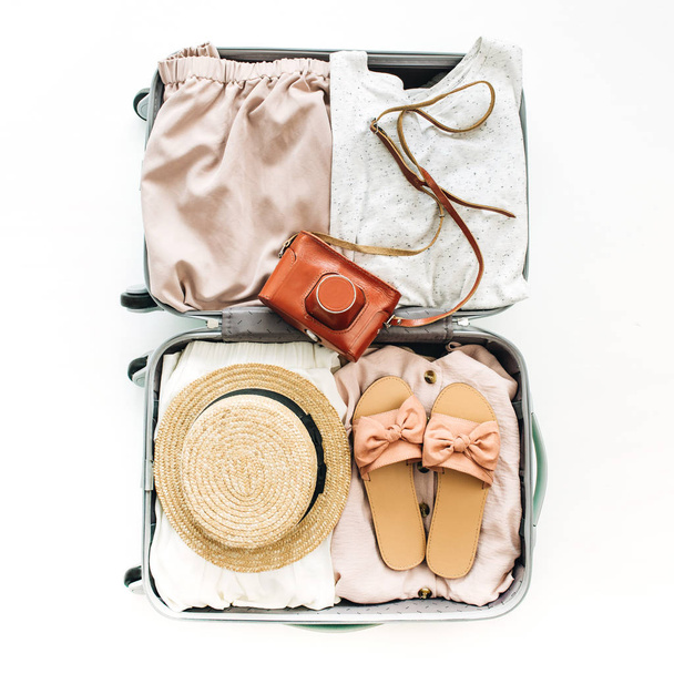 Příruční zavazadlo s stylové ženské oblečení na bílém pozadí. Pohled na ploché ležel, top. Letní cestování móda koncept. - Fotografie, Obrázek