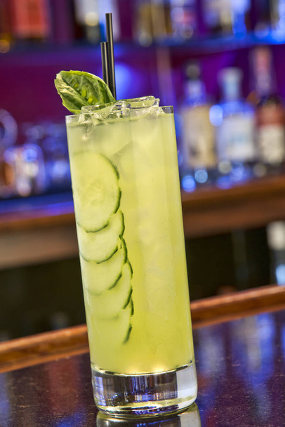 Cocktail with ice, cucumber slices and a mint garnish, sitting on a bar - Photo, image