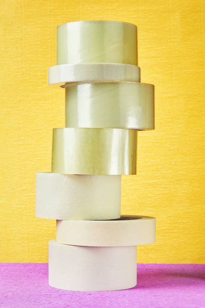 Set of scotch packing tape is stacked in form of tower, on yellow background. - Valokuva, kuva