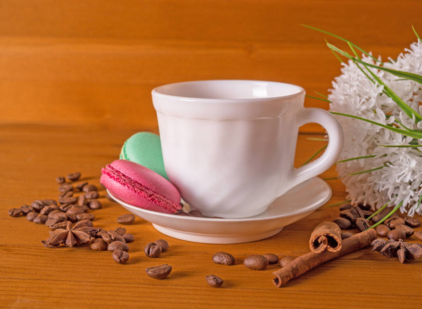 Cup, cakes, white bouquet of flowers, coffee grains and cinnamon sticks on a wooden table - Foto, immagini