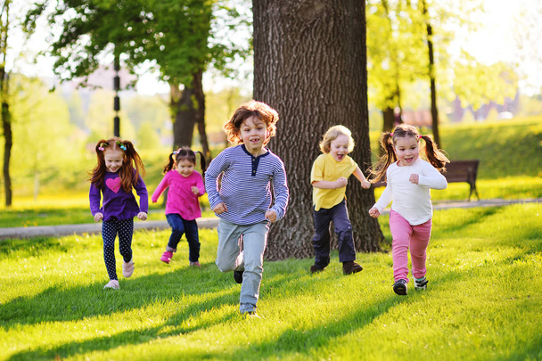 many young children smiling running along the grass in the park. - Фото, изображение