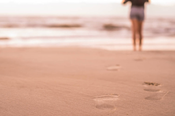 Woman walking on the beach, footprints in the sand. - Zdjęcie, obraz