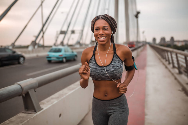 Fit african american woman running while listening to music through earphones - Photo, Image