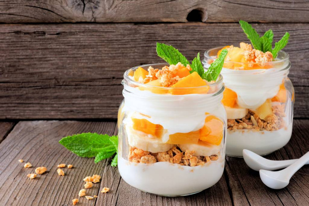 Healthy mango and pineapple parfaits in mason jars with a rustic wood background - Photo, Image