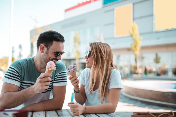 beautiful young couple are siting on a bench and eating ice-cream on the street - Фото, зображення