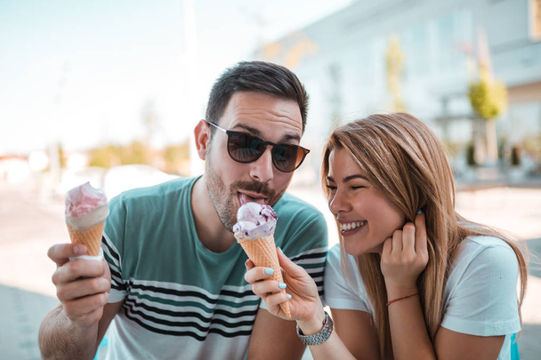 Young couple sharing ice cream while enjoying sunny weather outdoors - Fotó, kép