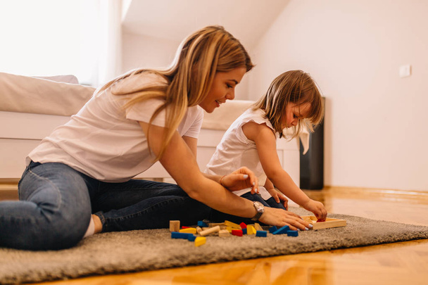 Νεαρή μητέρα και η κόρη της παίζουν με τα παιχνίδια σε ένα πάτωμα στο σπίτι - Φωτογραφία, εικόνα