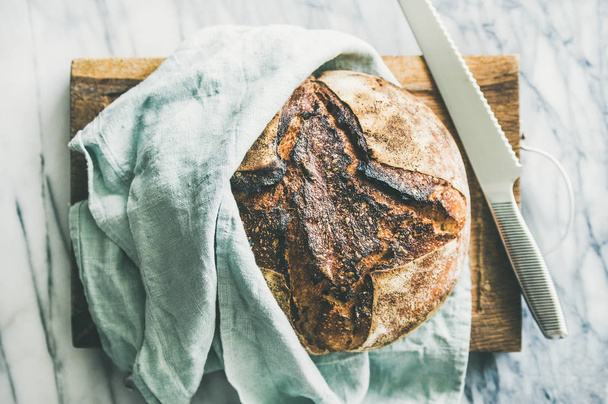 Freshly baked sourdough bread on rustic wooden chopping board over light grey marble background - 写真・画像