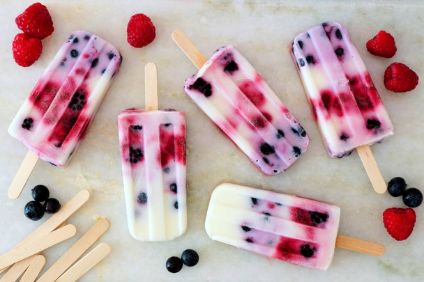 Healthy mixed berry yogurt popsicles with fruit on a white marble background - Фото, изображение