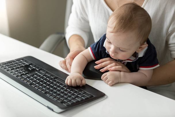 Retrato de bebé lindo niño escribiendo en el teclado de la computadora con la madre empresaria
 - Foto, imagen